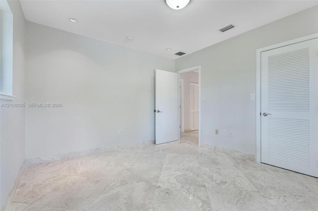 Neutral-toned stone tile flooring, recessed ceiling lighting, and louvered panel doors
