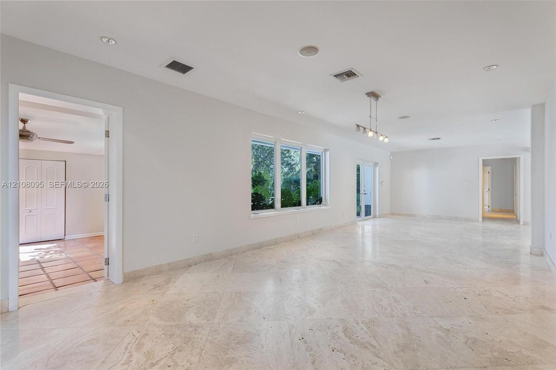 Open-concept interior featuring large-format stone tile flooring, recessed lighting, multi-pane windows, and a tiered linear chandelier