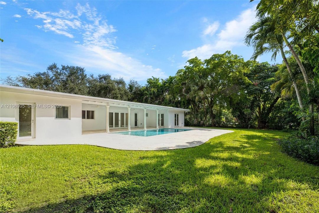 Exterior featuring a swimming pool, concrete patio, white facade, covered lanai with columns, and mature landscaping