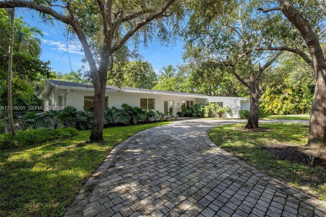 Single-story residence featuring a white exterior, a curved paver driveway, and mature landscaping