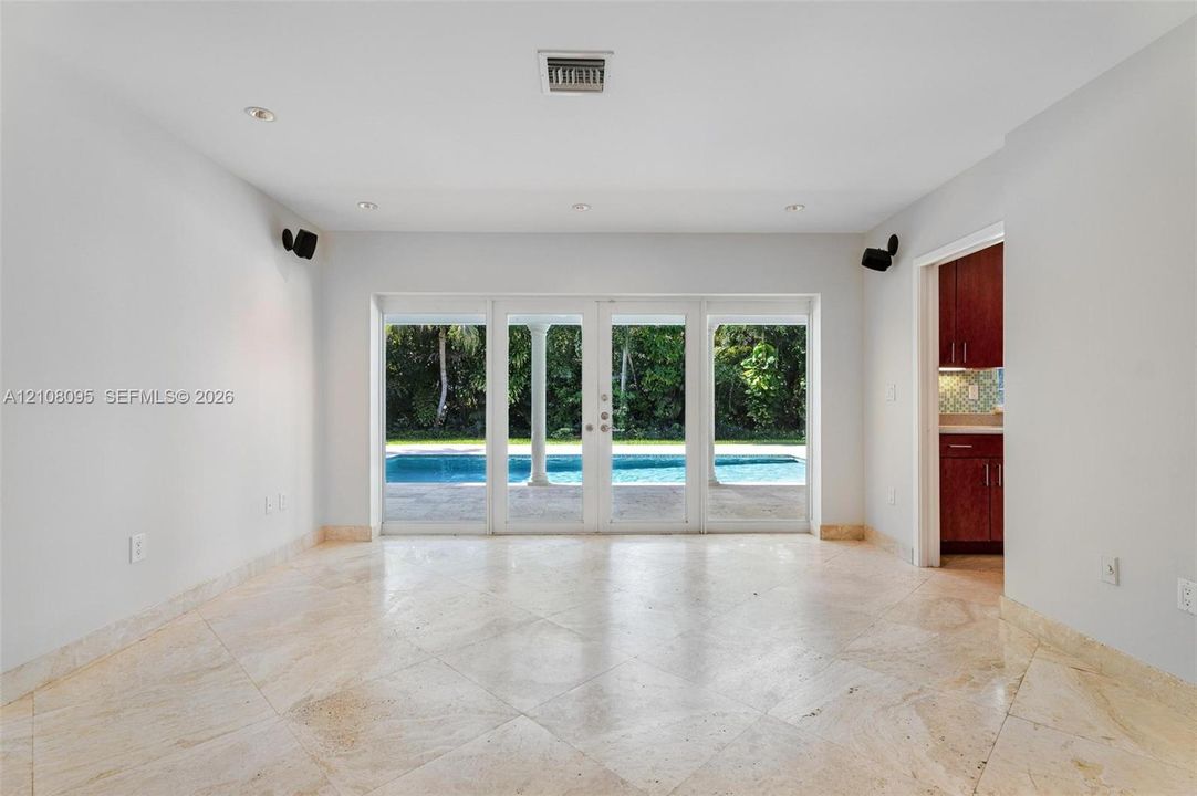 Interior space featuring large-format tile flooring, recessed lighting, and wall-mounted speakers, with four-panel glass doors opening to a pool and covered patio
