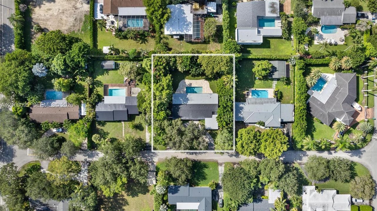 Aerial perspective of a property featuring an in-ground swimming pool, stone-finish pool deck, mature perimeter landscaping, and a rectangular roofline