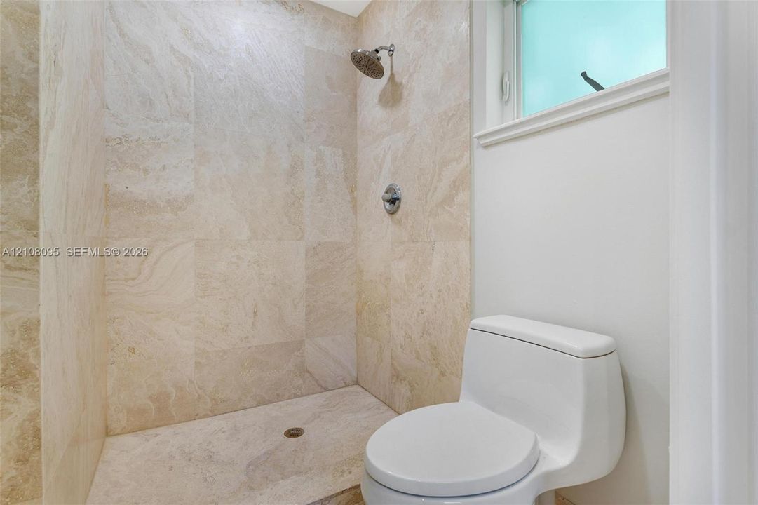 Walk-in shower featuring floor-to-ceiling stone tile surrounds, a circular shower head, and a one-piece white porcelain toilet