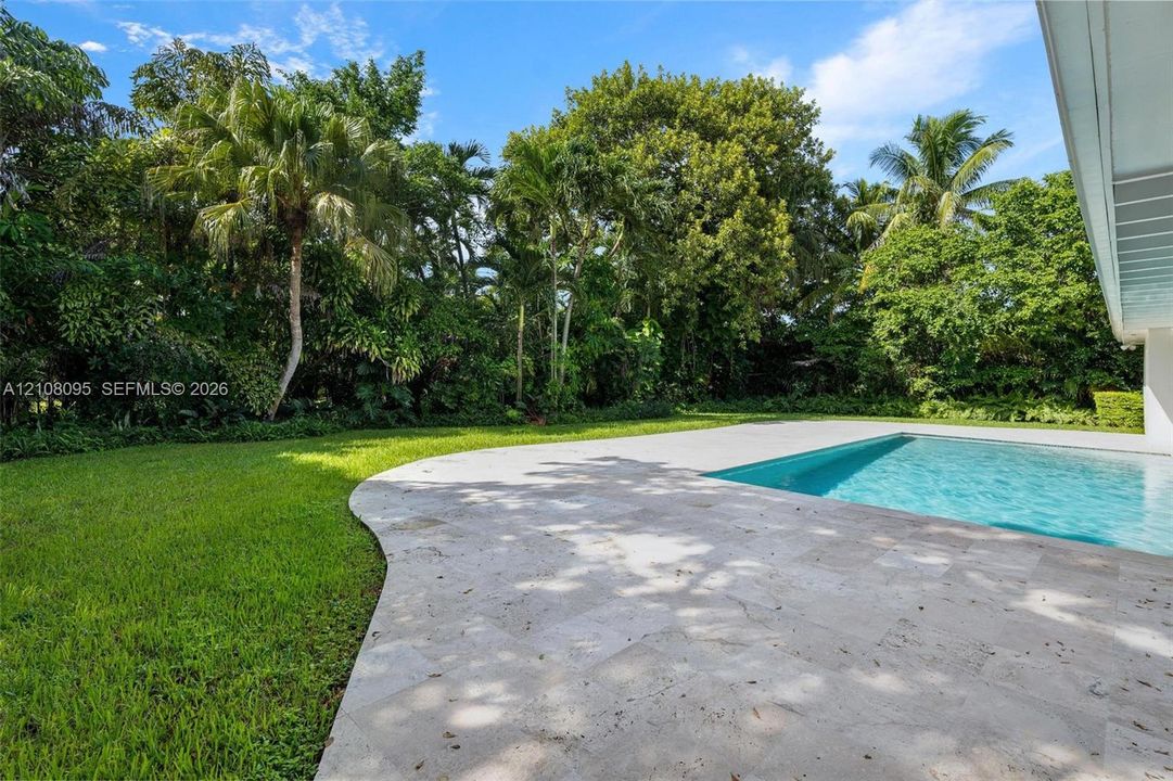 Backyard featuring a concrete-edged swimming pool, natural stone paver decking, manicured lawn, and mature perimeter landscaping