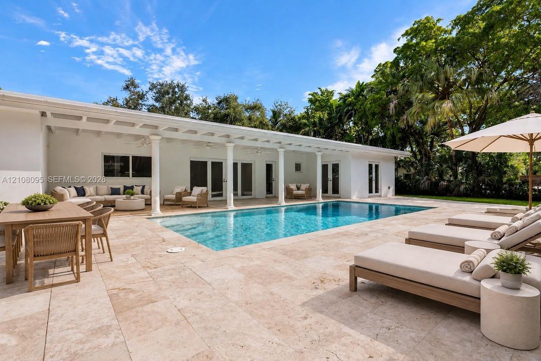 Backyard featuring a rectangular swimming pool, expansive stone patio, and a covered lanai supported by white columns
