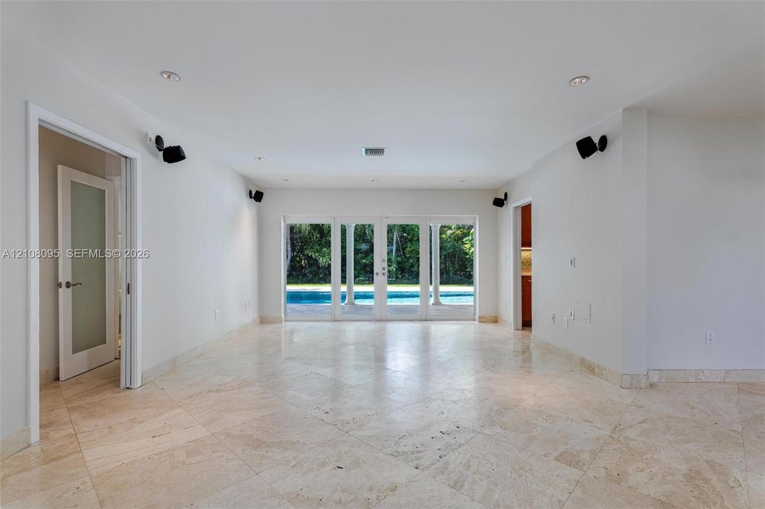 Open interior space featuring light-colored stone flooring, recessed lighting, and multi-panel glass doors with a perspective of an outdoor swimming pool
