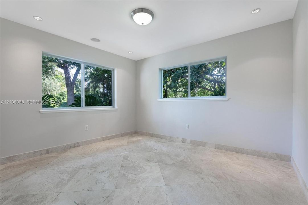 Neutral-toned interior space featuring light stone flooring, recessed ceiling lighting, and large sliding windows