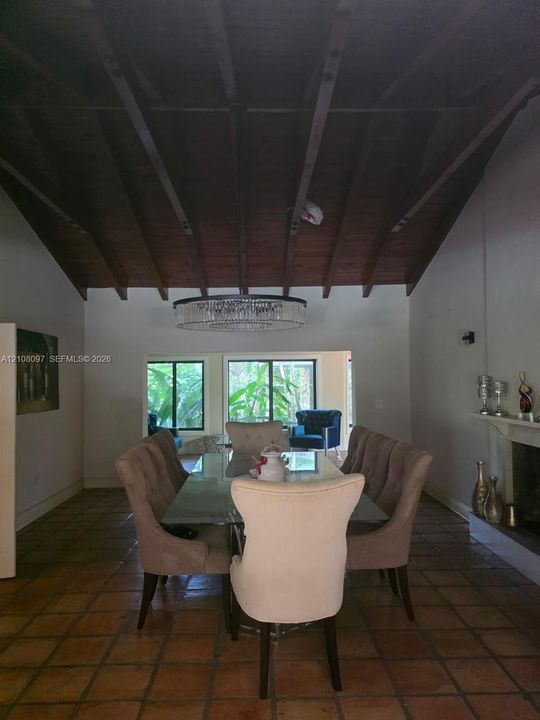 Vaulted ceiling with exposed wood beams, ceramic tile flooring, oversized circular chandelier, and a fireplace with a mantel