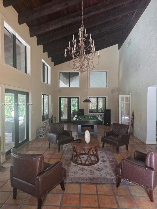 High vaulted ceilings with exposed dark wood beams, terracotta tile flooring, multi-light chandelier, and expansive windows