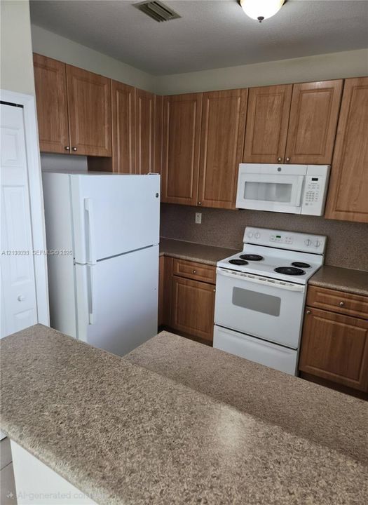 Kitchen featuring wood-finish cabinetry, solid surface countertops, white refrigerator, white electric range, and integrated over-the-range microwave