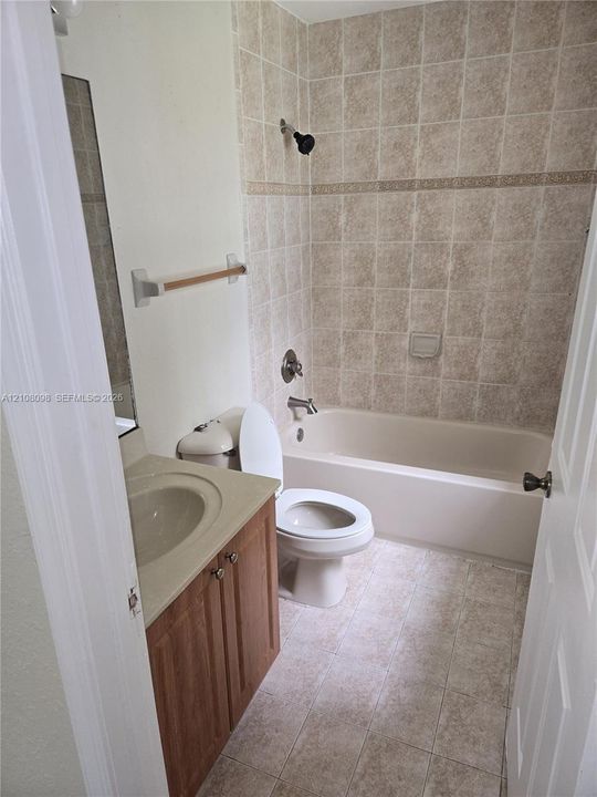 Bathroom featuring a wood-finish vanity with an integrated sink, a full-length wall mirror, and a tiled shower-tub combination with a decorative accent border