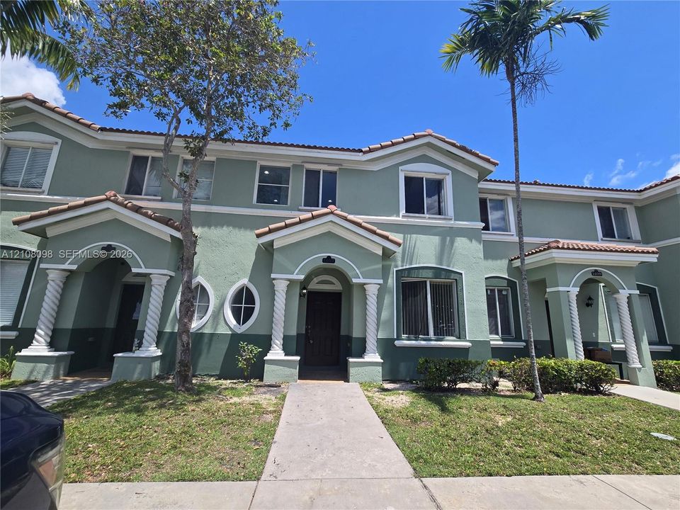 Two-story exterior featuring a stucco facade, covered entryway porches with spiral columns, decorative oval windows, and a multi-gabled tile roof