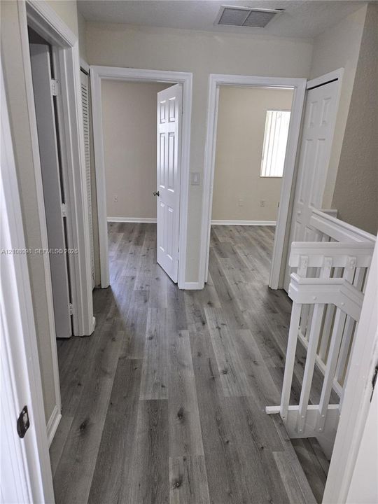 Hallway featuring wood-finish flooring, white paneled interior doors, and a painted wood staircase railing