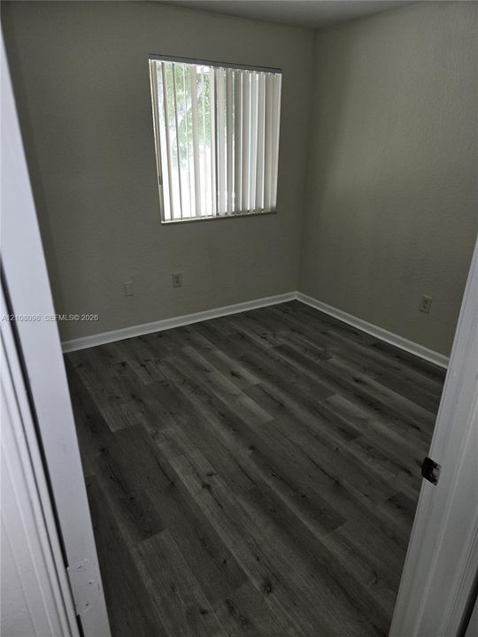 Interior space featuring wood-finish flooring, neutral wall paint, and a single window with vertical blinds