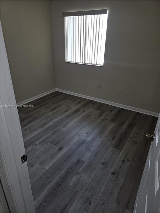 Room featuring wood-finish flooring, neutral wall paint, and a window with vertical blinds
