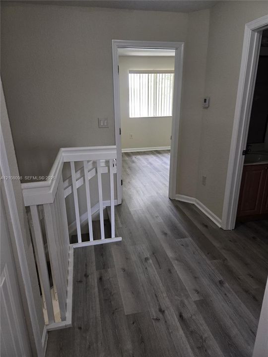 Hallway featuring wood-finish flooring, white wooden stair railings, and solid core interior doors