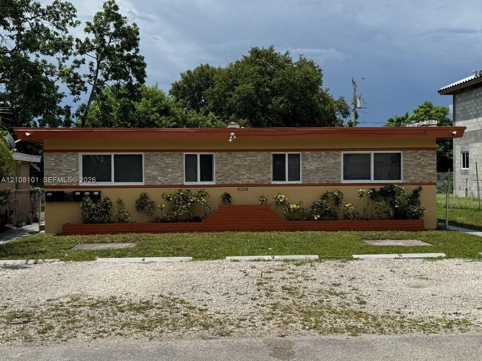 Single-story exterior featuring a stone-veneer facade, flat roofline, integrated brick planters, and designated gravel parking spaces