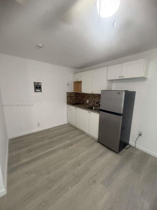 Kitchen featuring wood-finish flooring, white cabinetry, a multi-tonal decorative tile backsplash, and a stainless steel refrigerator