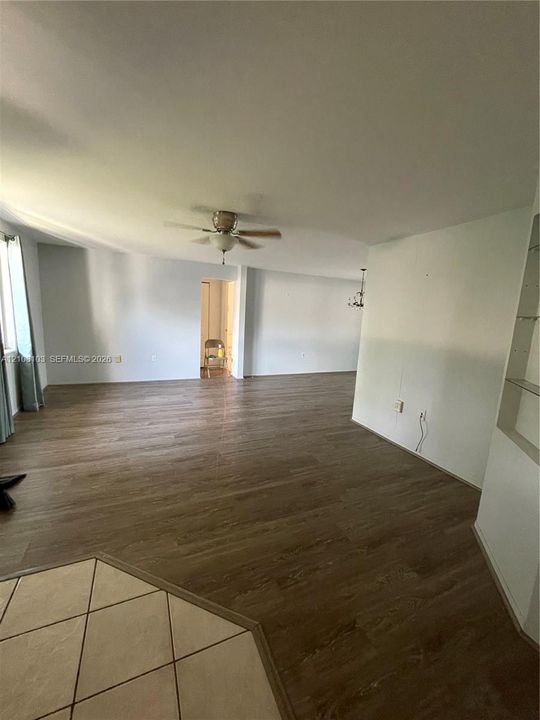 Open-concept interior featuring wood-finish flooring, a ceiling fan, neutral wall paint, and built-in shelving with glass inserts
