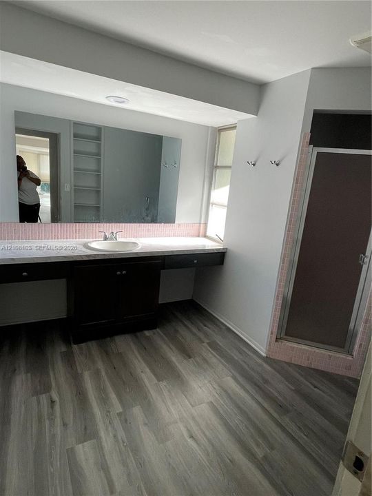 Floating vanity featuring a stone-finish countertop, recessed lighting, integrated wall shelving, wood-finish flooring, and a walk-in shower with tiled surround