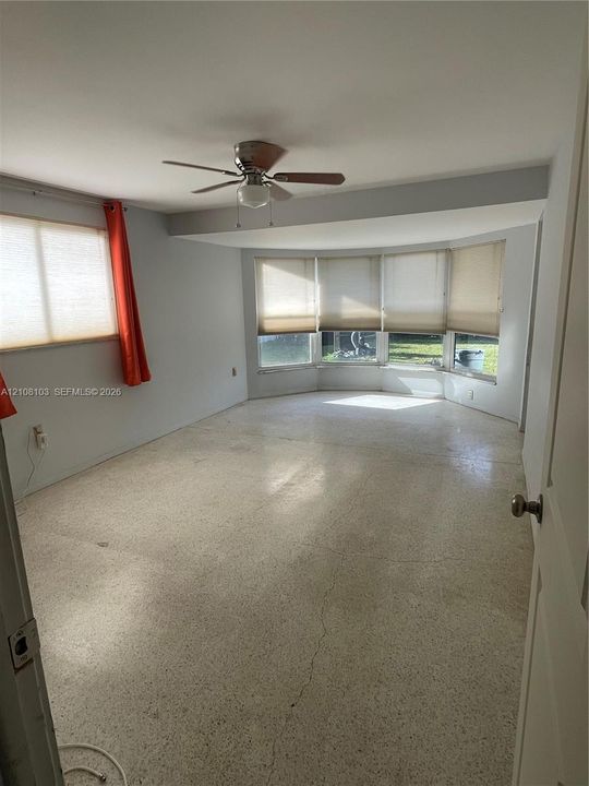 Spacious room featuring a bay window, neutral flooring, and a ceiling fan
