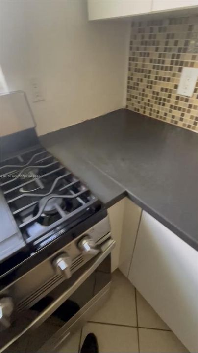 Stainless steel gas range featuring a multi-burner cooktop, solid-surface countertop, mosaic tile backsplash, and white cabinetry