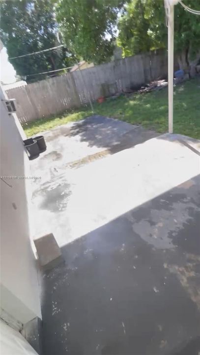 Concrete patio featuring a covered area with a support post, fenced rear yard, and mature trees
