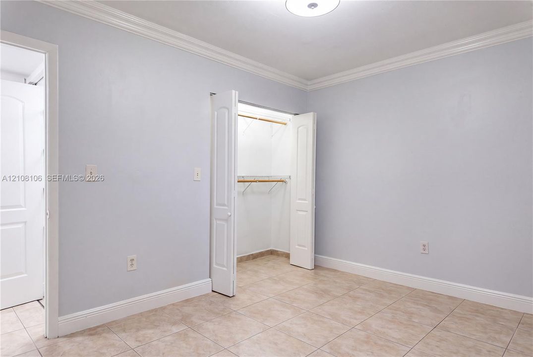 Ceramic tile flooring, crown molding, and a closet with bifold doors and built-in shelving