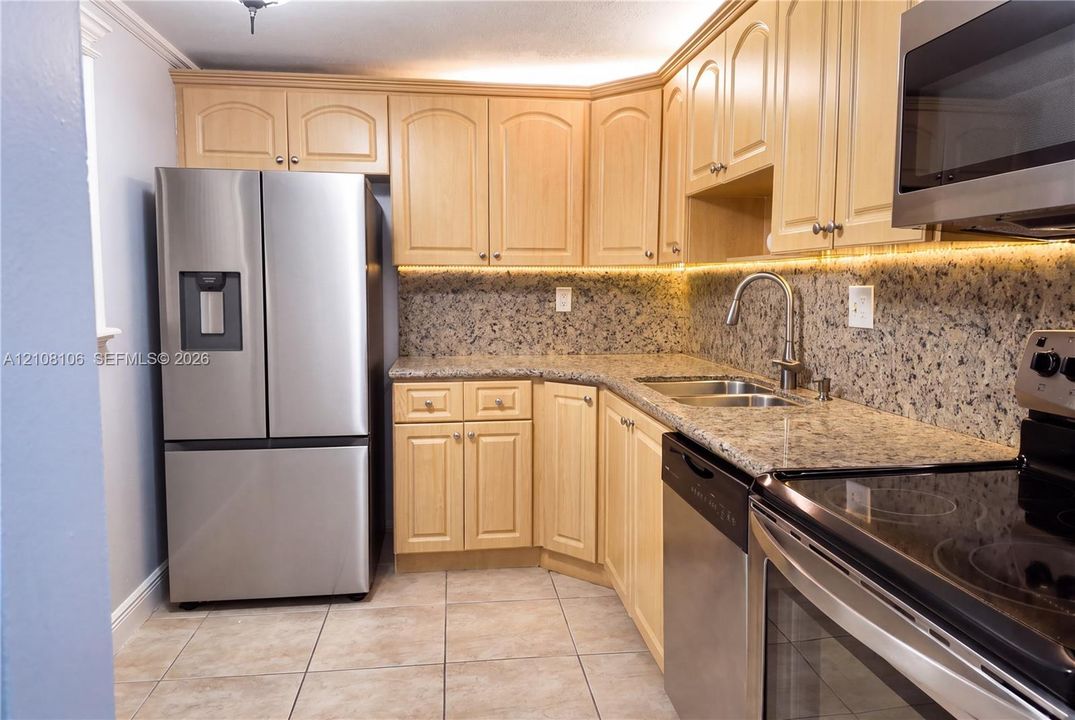 Kitchen featuring light-finish cabinetry, stone-texture countertops, stainless steel appliances, under-cabinet lighting, and tile flooring