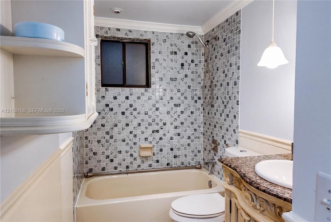 Bathroom featuring a patterned mosaic tile shower surround, integrated bathtub, vanity with stone-finish countertop, undermount sink, and wall-mounted pendant lighting