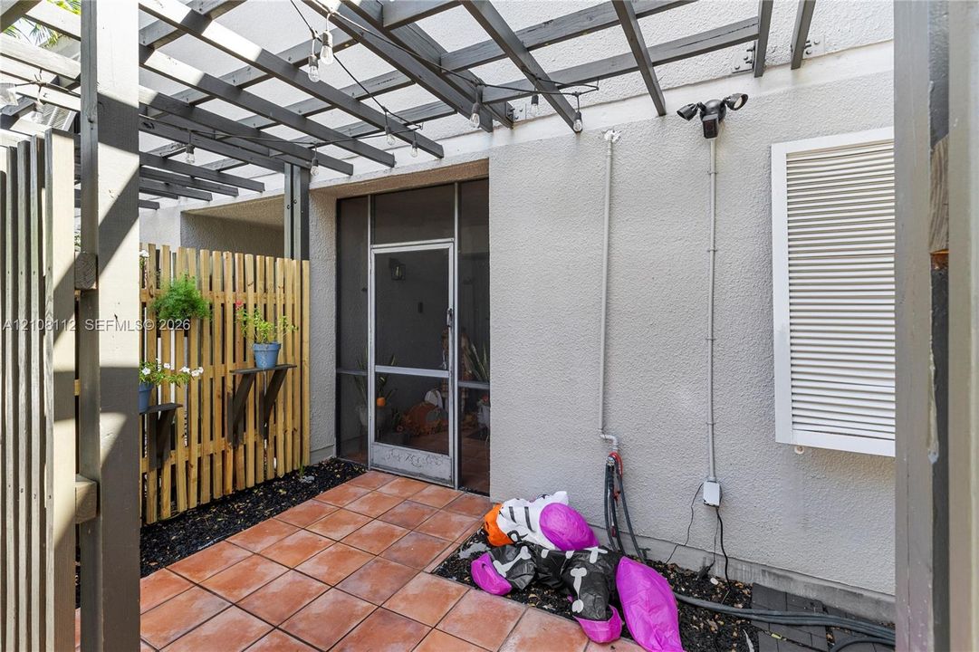 Outdoor patio featuring a wooden pergola, terracotta tile flooring, vertical slat wood privacy screen, and a screened entry door
