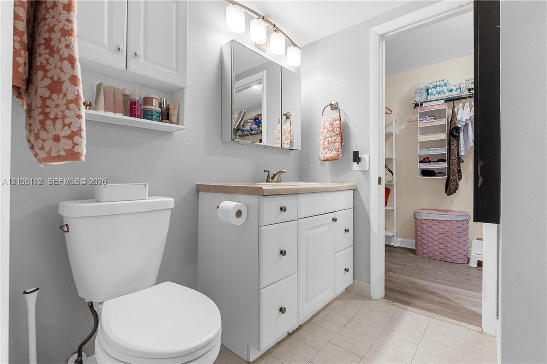 Bathroom featuring white cabinetry, a tri-panel medicine cabinet, wall-mounted light fixture, and solid surface countertop with an integrated sink