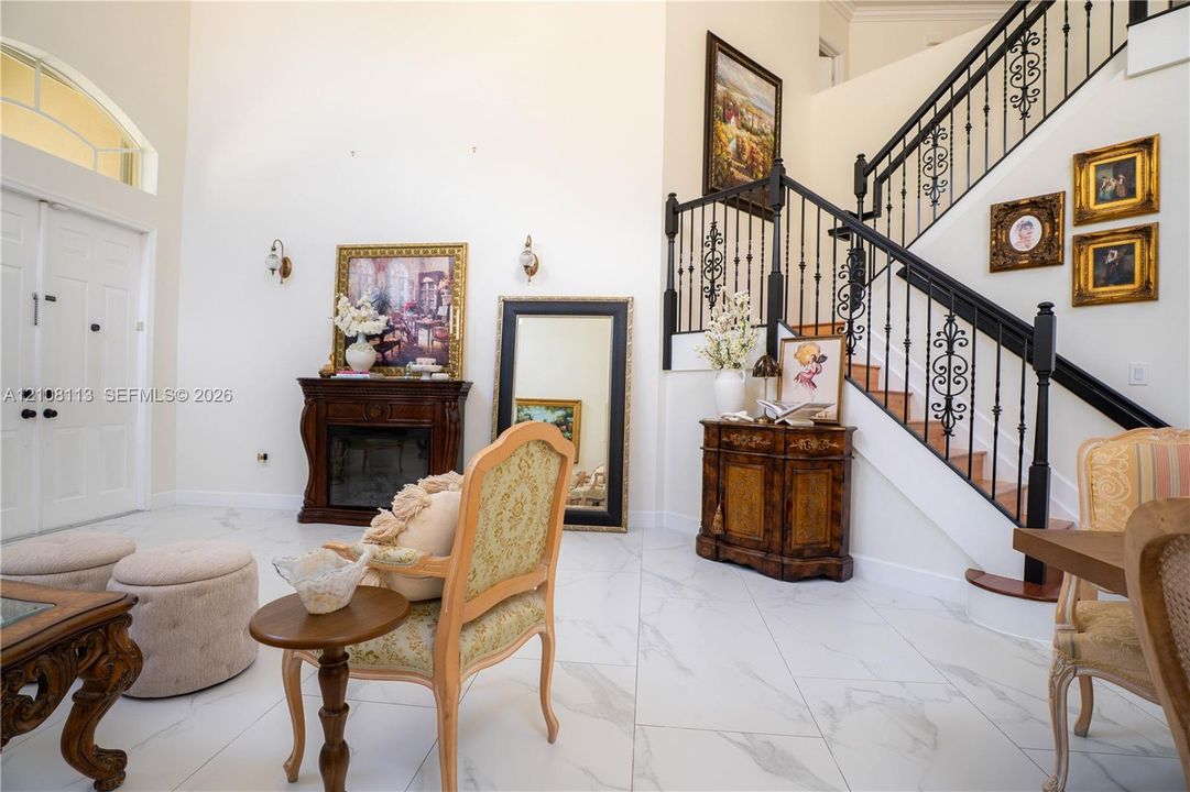 Grand entry featuring double front doors, vaulted ceilings, light-toned stone-finish tile flooring, a staircase with decorative wrought-iron railings, and an integrated dark wood-finish fireplace
