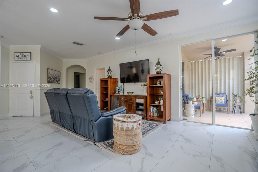 Large-format tile flooring, recessed ceiling lighting, central ceiling fan, and sliding glass doors providing external access