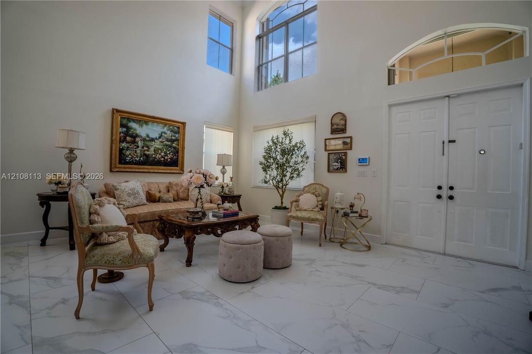 Double-height ceilings featuring expansive windows with an arched transom, double-door entry, and large-format tile flooring with marble-pattern veining