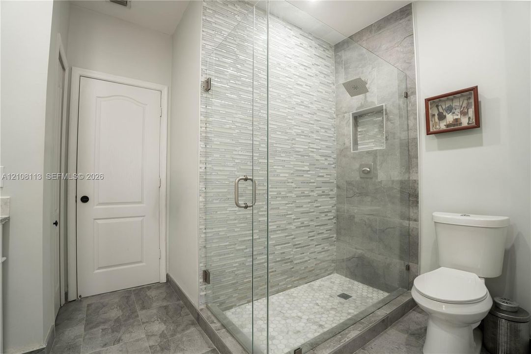 Walk-in shower featuring a frameless glass enclosure, stacked stone accent wall, inset wall niche, and hexagon tile floor