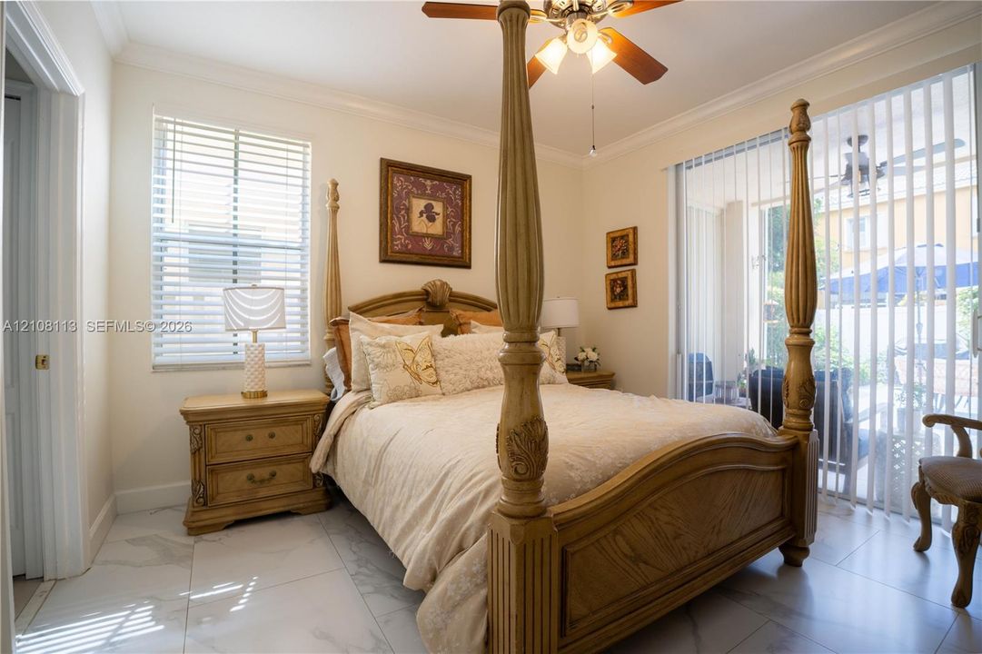 Large-format tile flooring, crown molding, ceiling fan with integrated lighting, and sliding glass doors with vertical blinds