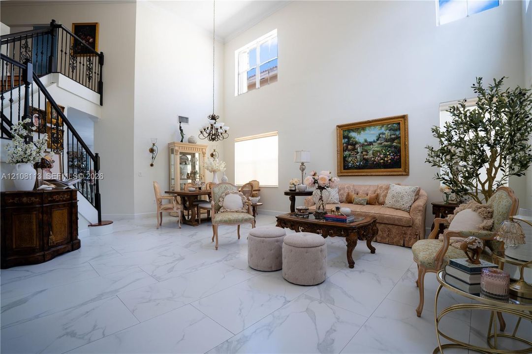 Two-story ceiling height, large-format tile flooring with marble-finish veining, grand staircase with wrought-iron balusters, multi-level windows, and a central tiered chandelier