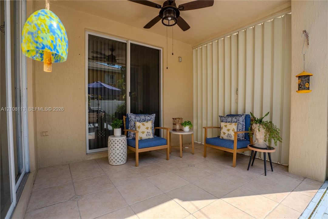 Covered patio featuring large-format tile flooring, a ceiling fan, and sliding glass entry doors with vertical blinds