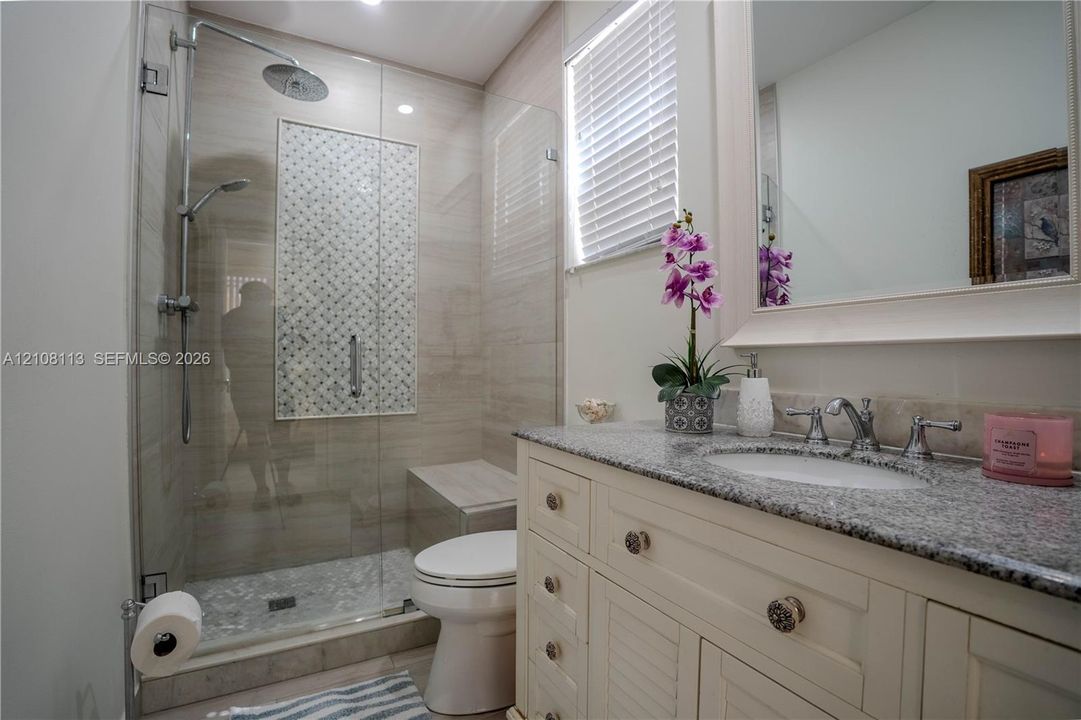 Bathroom featuring a vanity with stone-finish countertop, undermount sink, walk-in glass-enclosed shower with tiled accent inlay, and built-in shower bench