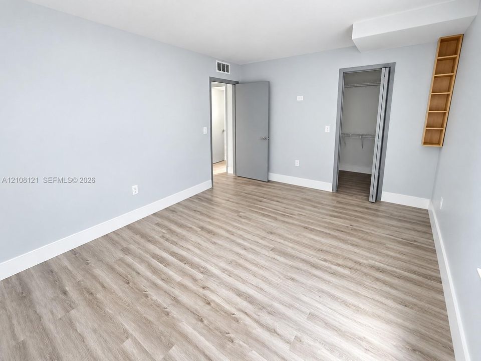 Wood-finish flooring, neutral wall tones, built-in wall shelving, and a walk-in closet with integrated wire storage