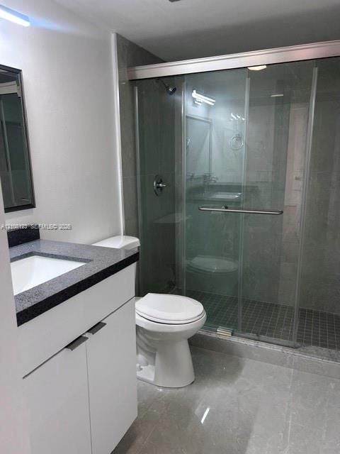 Bathroom featuring a floating vanity with dark-toned countertop, under-mount sink, sliding glass shower enclosure, and oversized floor tiles