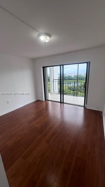 Room featuring wood-finish flooring, a neutral color palette, and sliding glass doors leading to a private balcony with metal railings and water scenery
