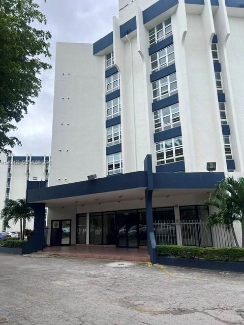 Multi-story building exterior featuring vertical concrete architectural accents, white stucco finish with blue contrast trim, and ground-level glass entrance