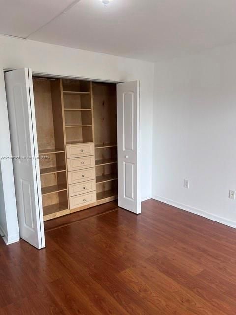 Room featuring wood-finish flooring and a closet with custom built-in shelving and integrated drawers