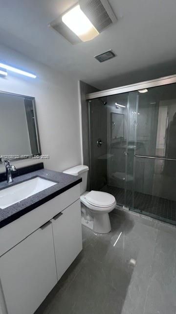 Bathroom featuring a vanity with a dark-toned countertop, under-mount sink, chrome faucet, glass-enclosed shower, and large-format tile flooring
