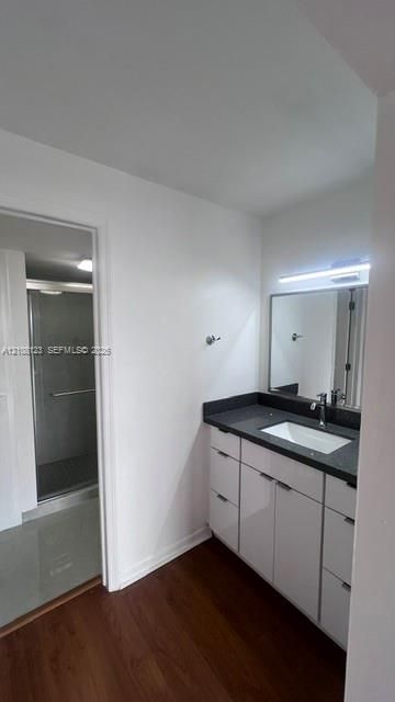 Modern vanity featuring a dark stone countertop, integrated rectangular sink, glossy white cabinetry, and a wall-mounted light fixture above the mirror