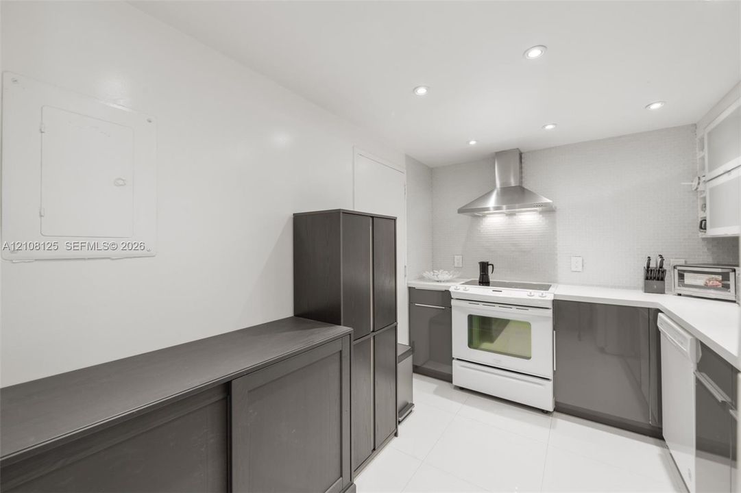 Kitchen featuring dark-toned cabinetry, white countertops, stainless steel range hood, built-in range, and recessed ceiling lighting