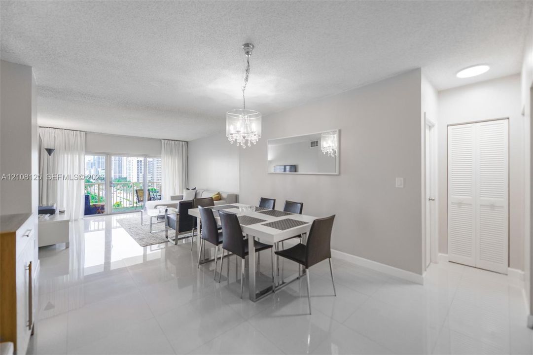 Open-concept living space featuring high-gloss tile flooring, an ornate crystal chandelier, a large wall-mounted mirror, and white louvered-panel closet doors