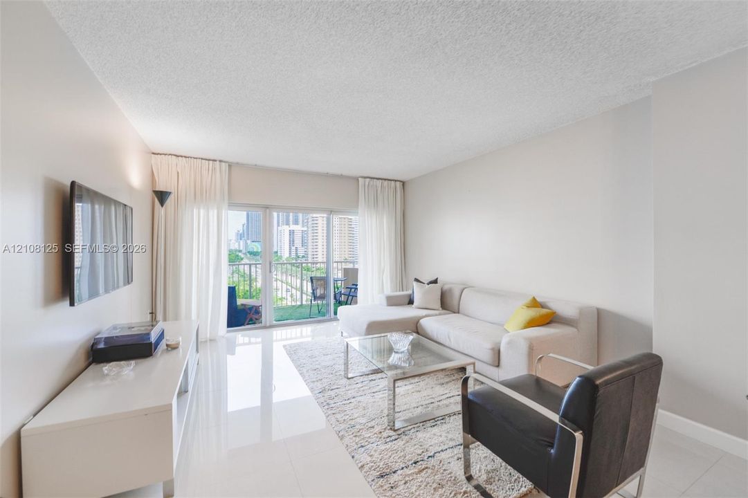 Living area featuring light-toned tile flooring, neutral wall paint, and floor-to-ceiling glass sliding doors providing access to an exterior balcony